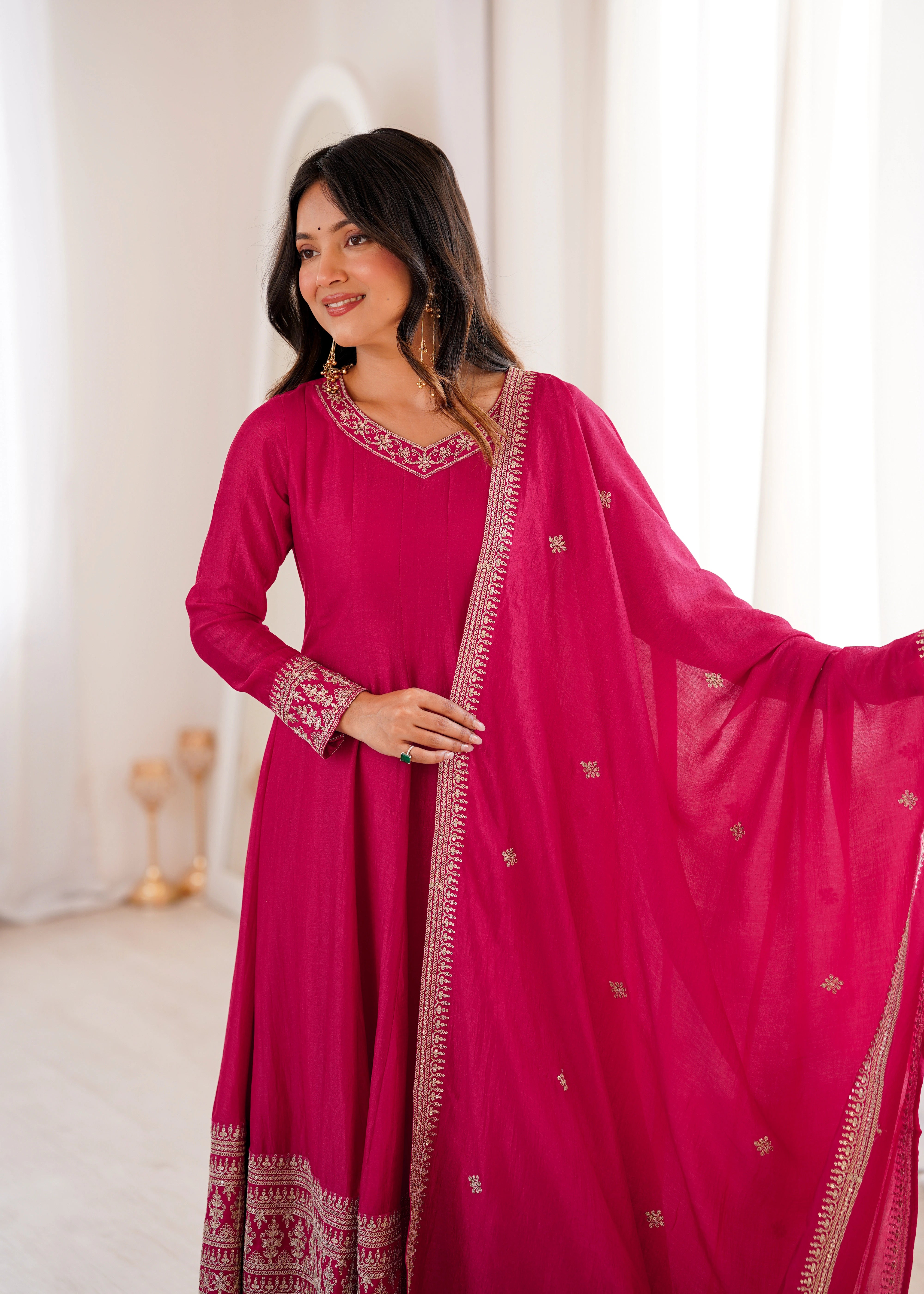 Woman wearing a pink traditional outfit with intricate designs in a softly lit room.
