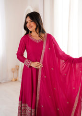 Woman wearing a pink traditional outfit with intricate designs in a softly lit room.