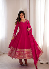 Woman wearing a vibrant pink traditional outfit with intricate patterns in a softly lit room.