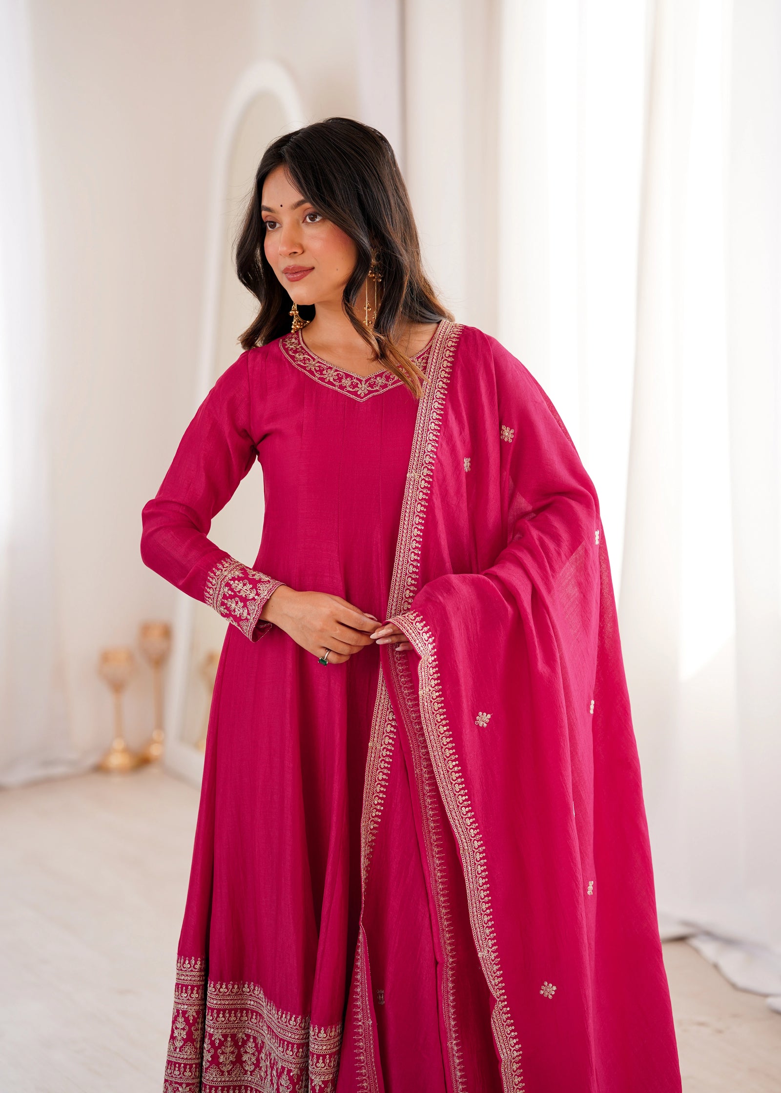 Woman wearing a pink traditional outfit with intricate designs indoors.