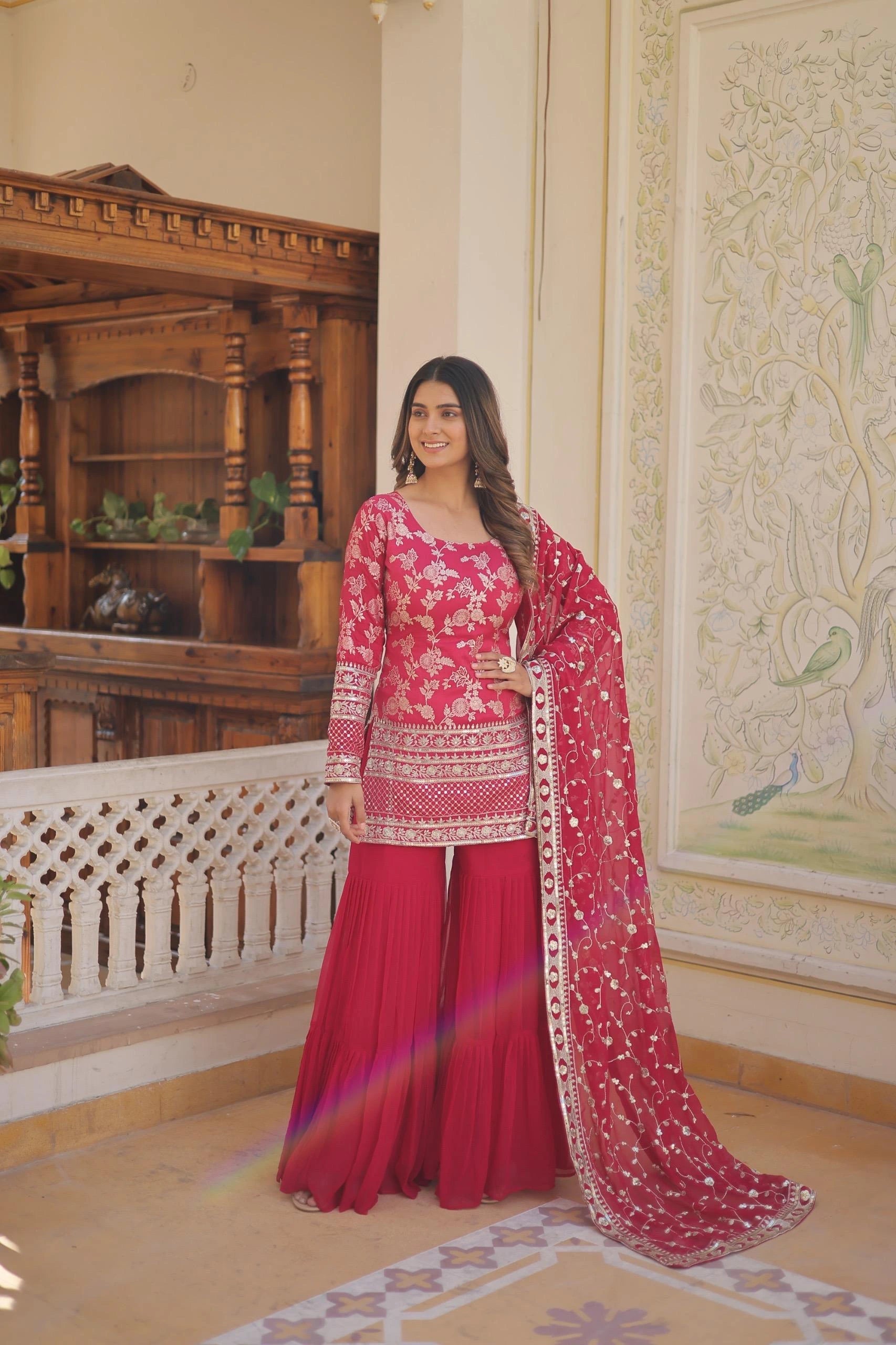 Woman in a red traditional outfit with floral patterns in an ornate room.