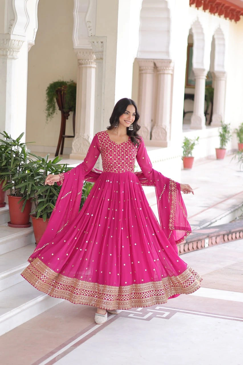 Woman in a pink traditional outfit standing in an elegant indoor setting with white marble floors and columns.
