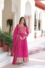 Woman in a pink traditional outfit standing in an elegant indoor setting with plants.