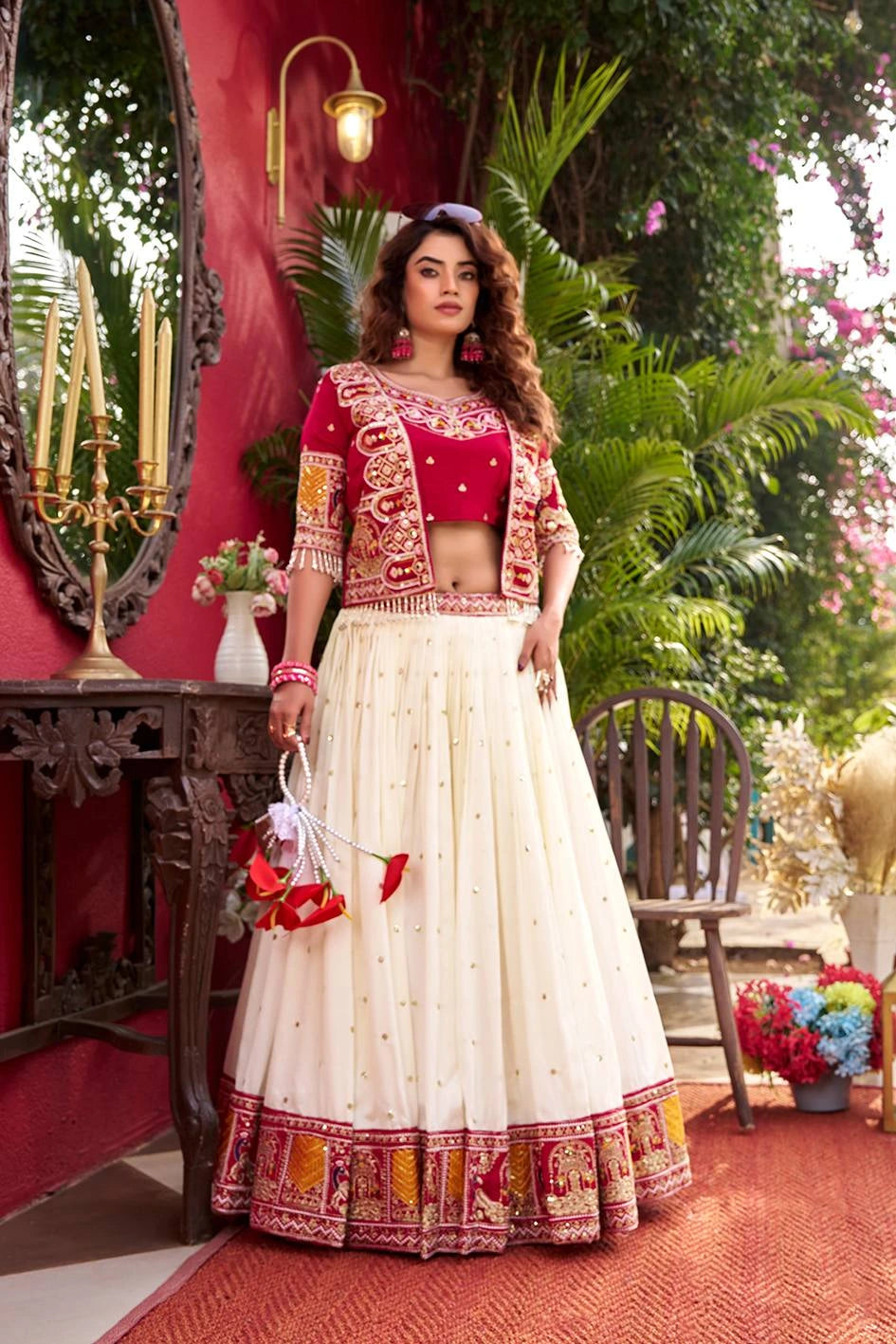 Woman in a traditional outfit standing in an outdoor setting with greenery and decor.