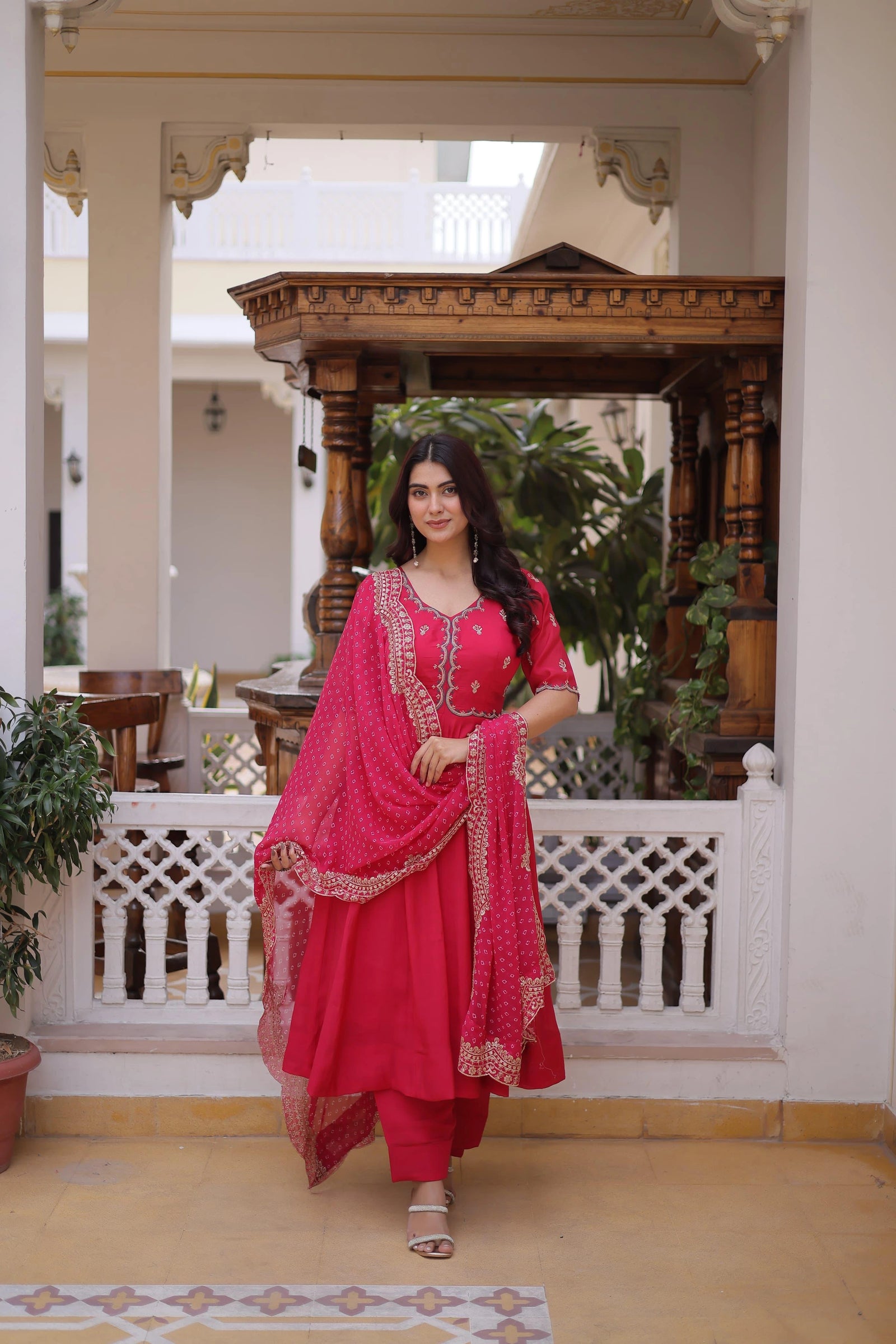 Woman in a pink traditional outfit standing in an elegant indoor setting with wooden architecture.