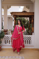 Woman in a pink traditional outfit standing in an elegant indoor setting with wooden architecture.