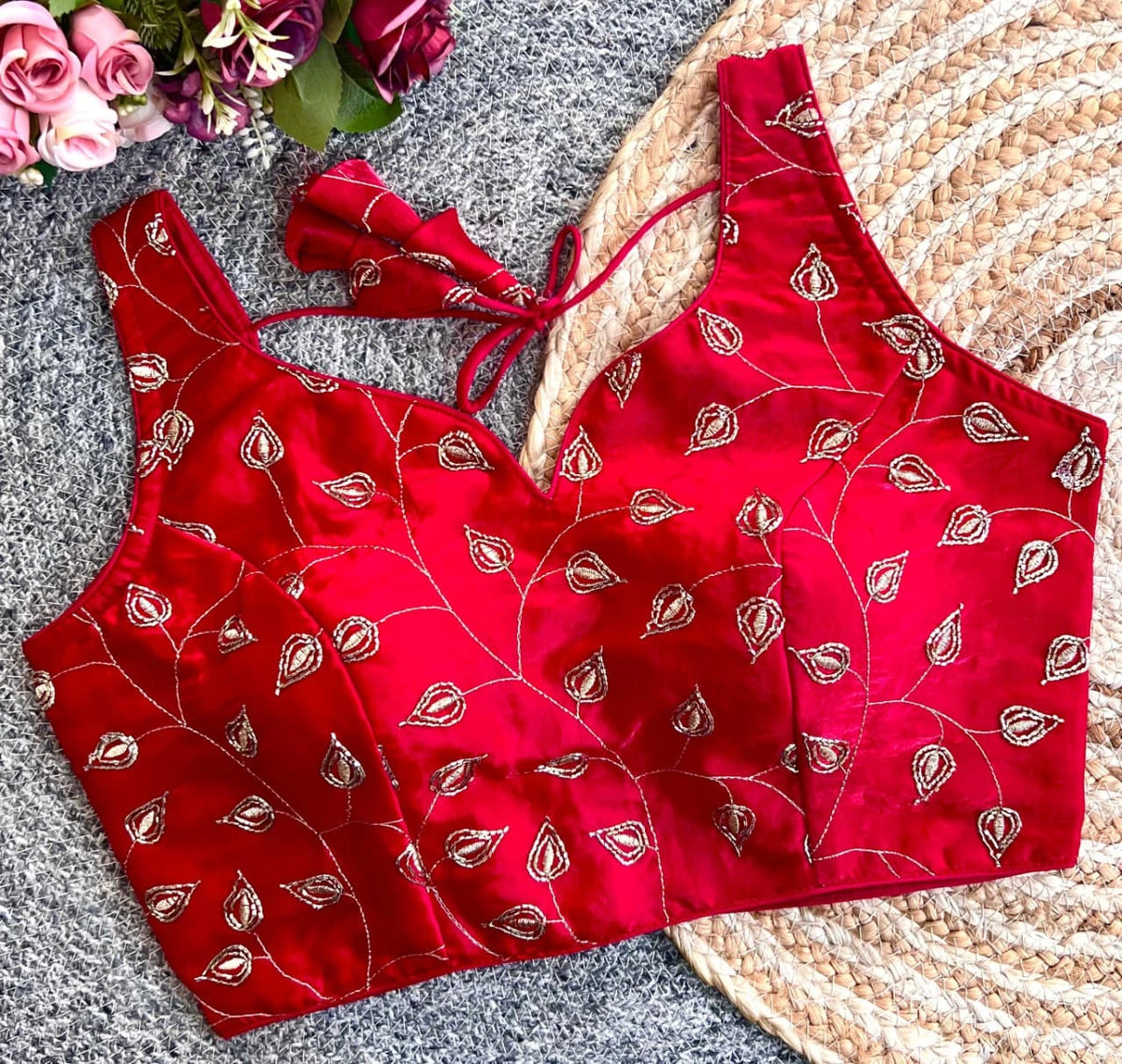 Red blouse with gold patterns on a textured surface with flowers in the corner