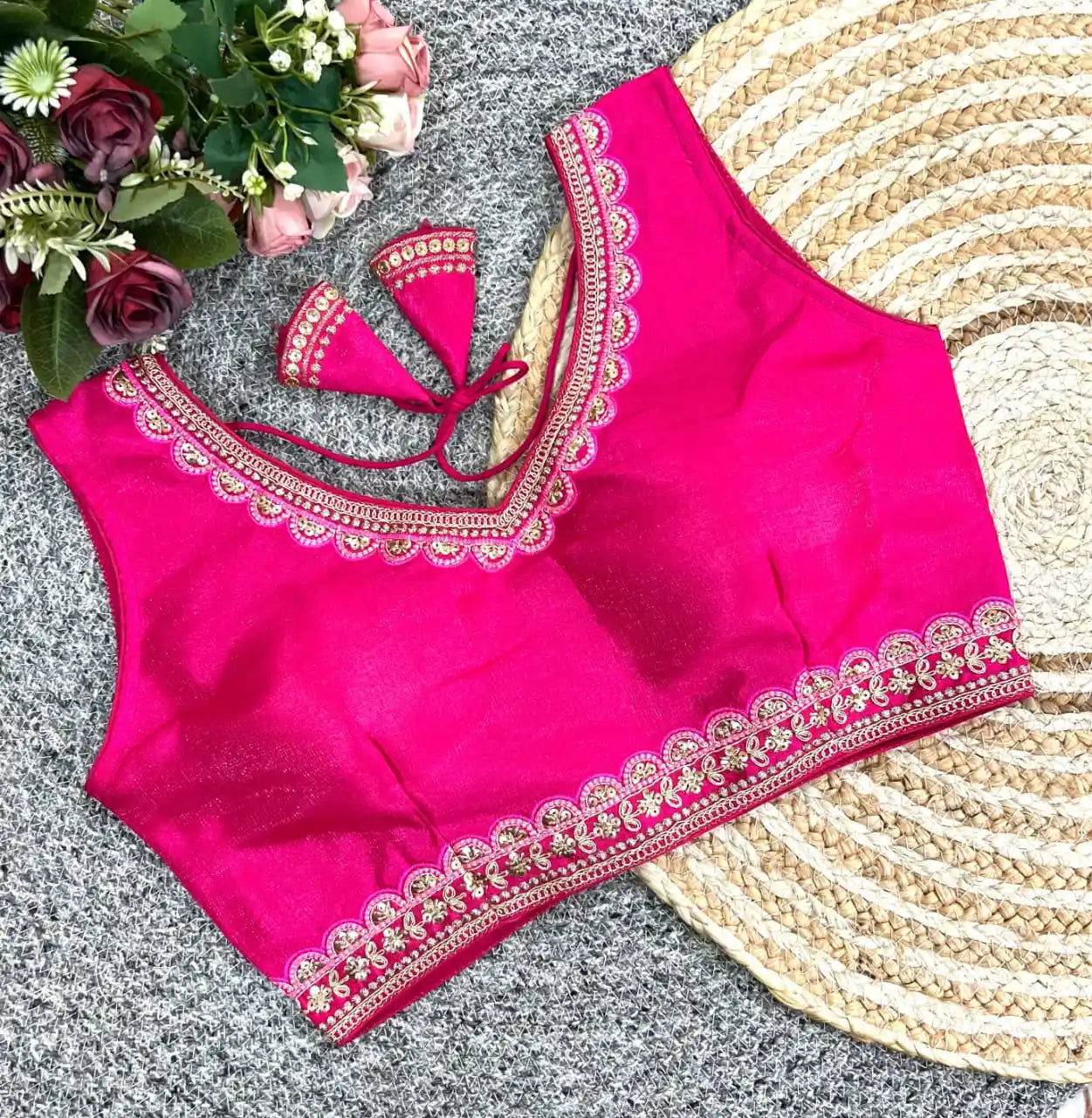 Pink blouse with intricate embroidery on a textured surface with flowers and a hat.