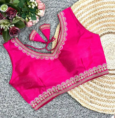 Pink blouse with intricate embroidery on a textured surface with flowers and a hat.