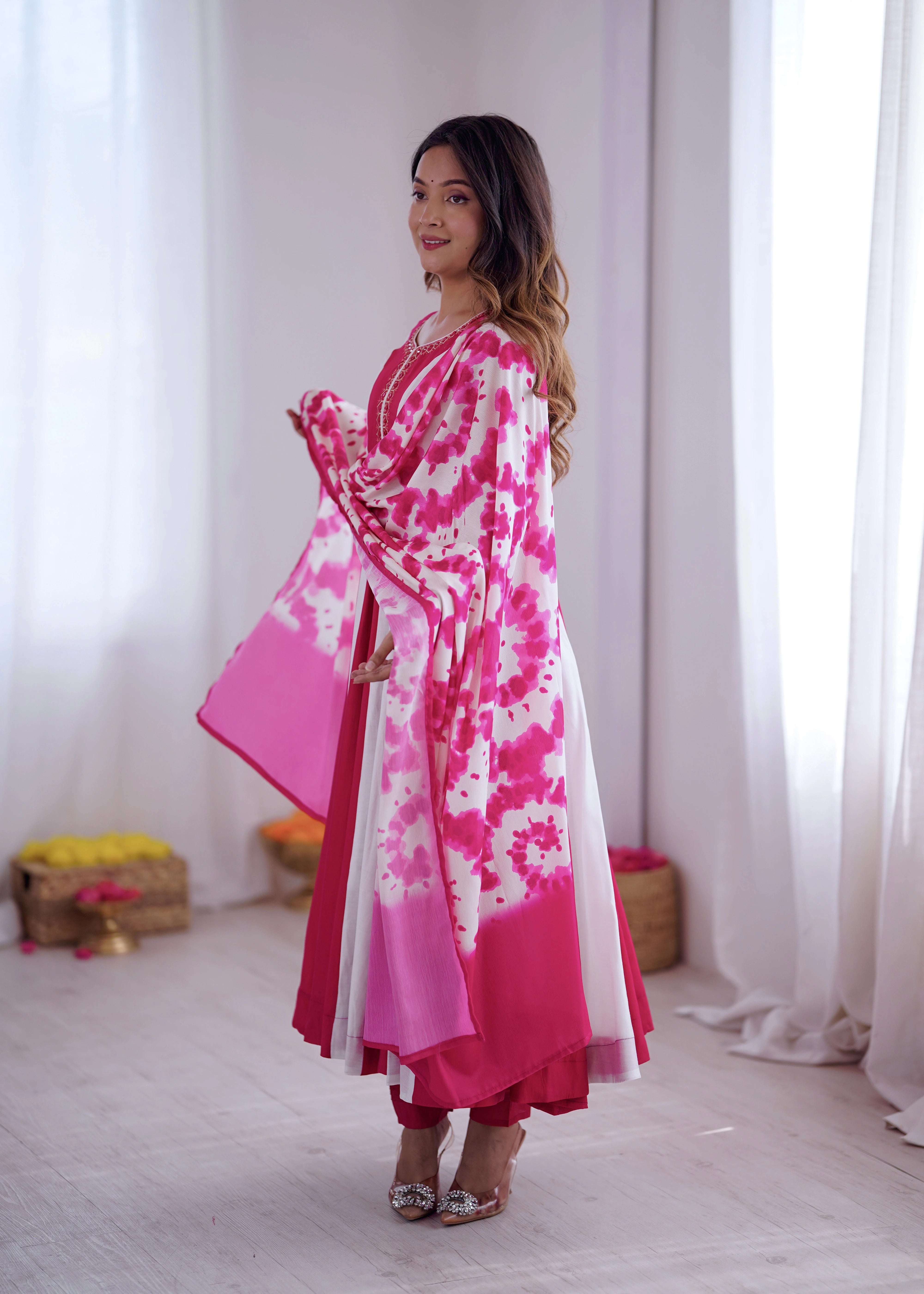 Woman wearing a pink and white floral dress standing in a room with white curtains.