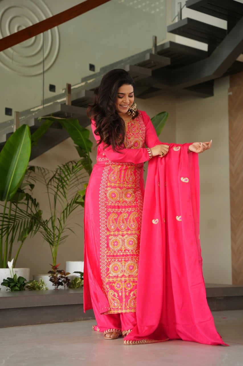 Woman in a bright pink traditional outfit with gold patterns indoors.