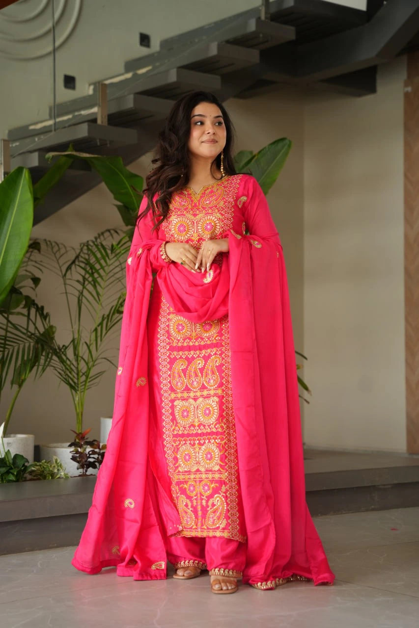 Woman in a pink traditional outfit with intricate patterns standing indoors.