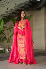 Woman in a pink traditional outfit with intricate patterns standing indoors.
