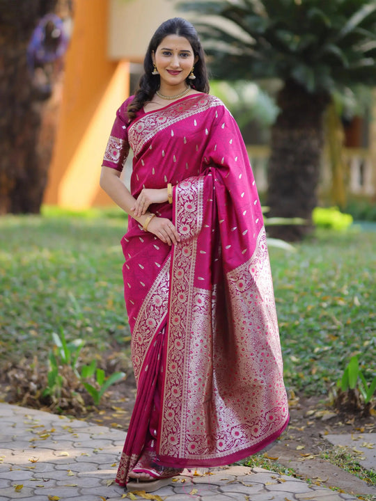 Woman wearing a pink saree with a pattern, standing outdoors on a path with greenery.