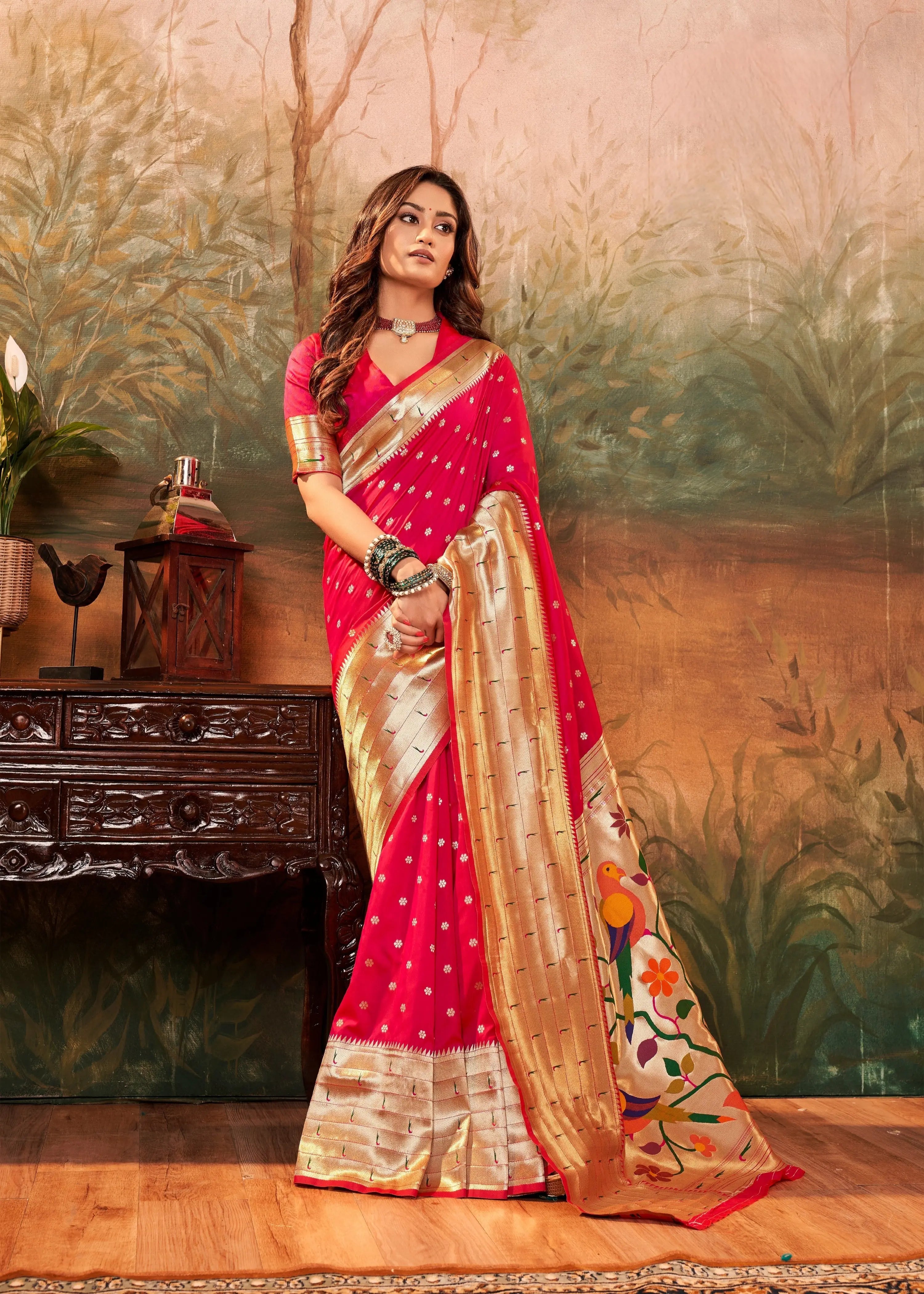 Woman in a red and gold saree standing in front of a decorative wall.