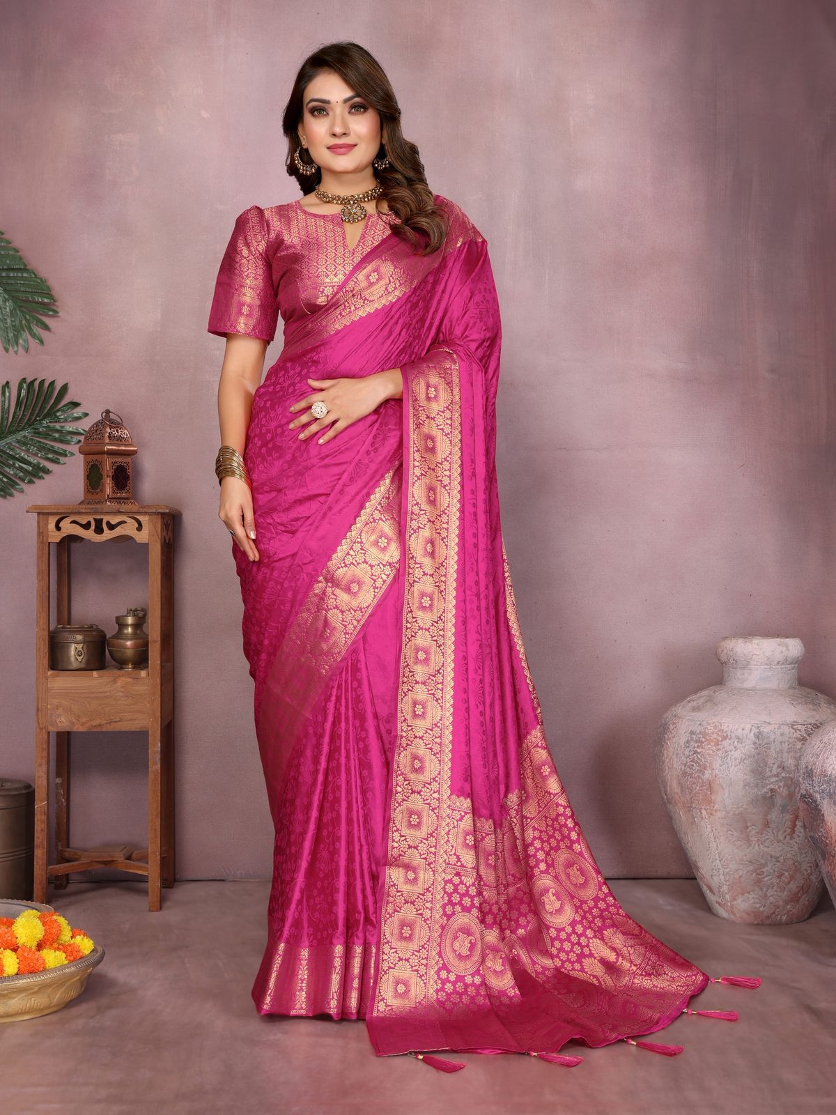 Woman wearing a pink saree with gold patterns in a decorative setting.