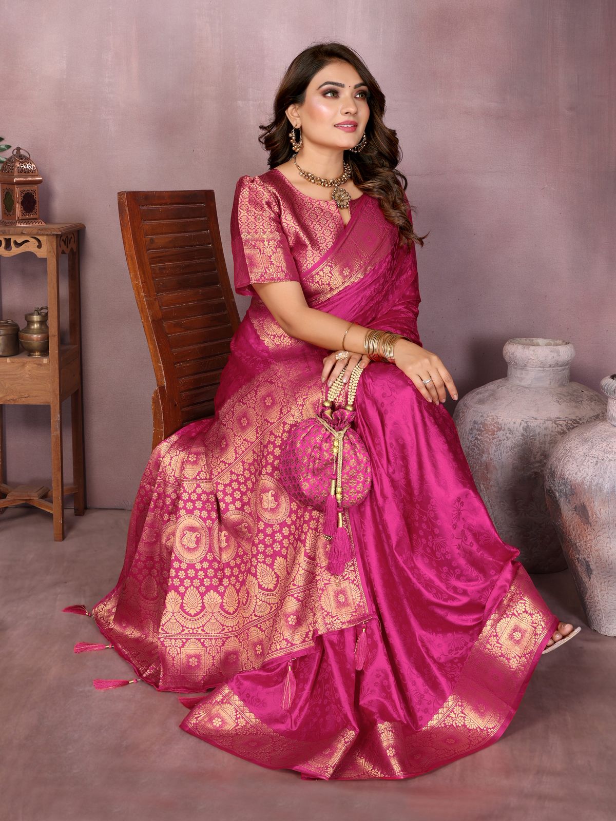 Woman in a pink saree sitting on a chair against a plain background