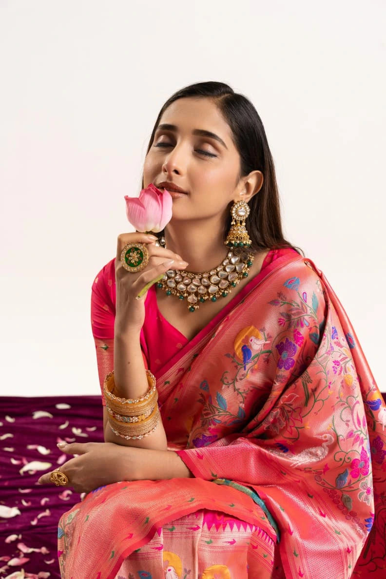 Woman in a traditional saree holding a pink flower against a white background