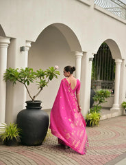 Woman in a pink saree walking in a courtyard with white columns and potted plants.