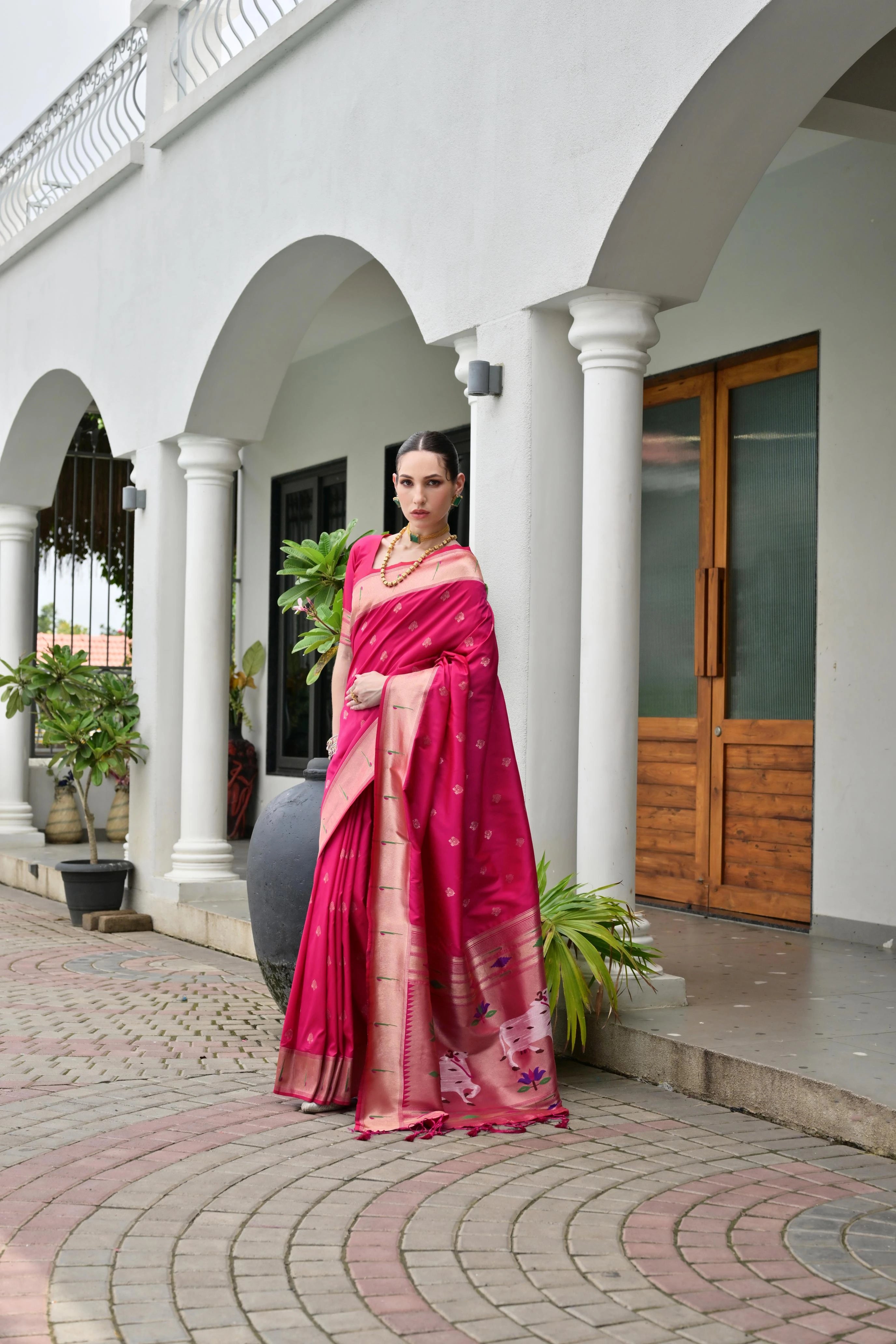 Woman in a pink saree standing in front of a white building with columns.
