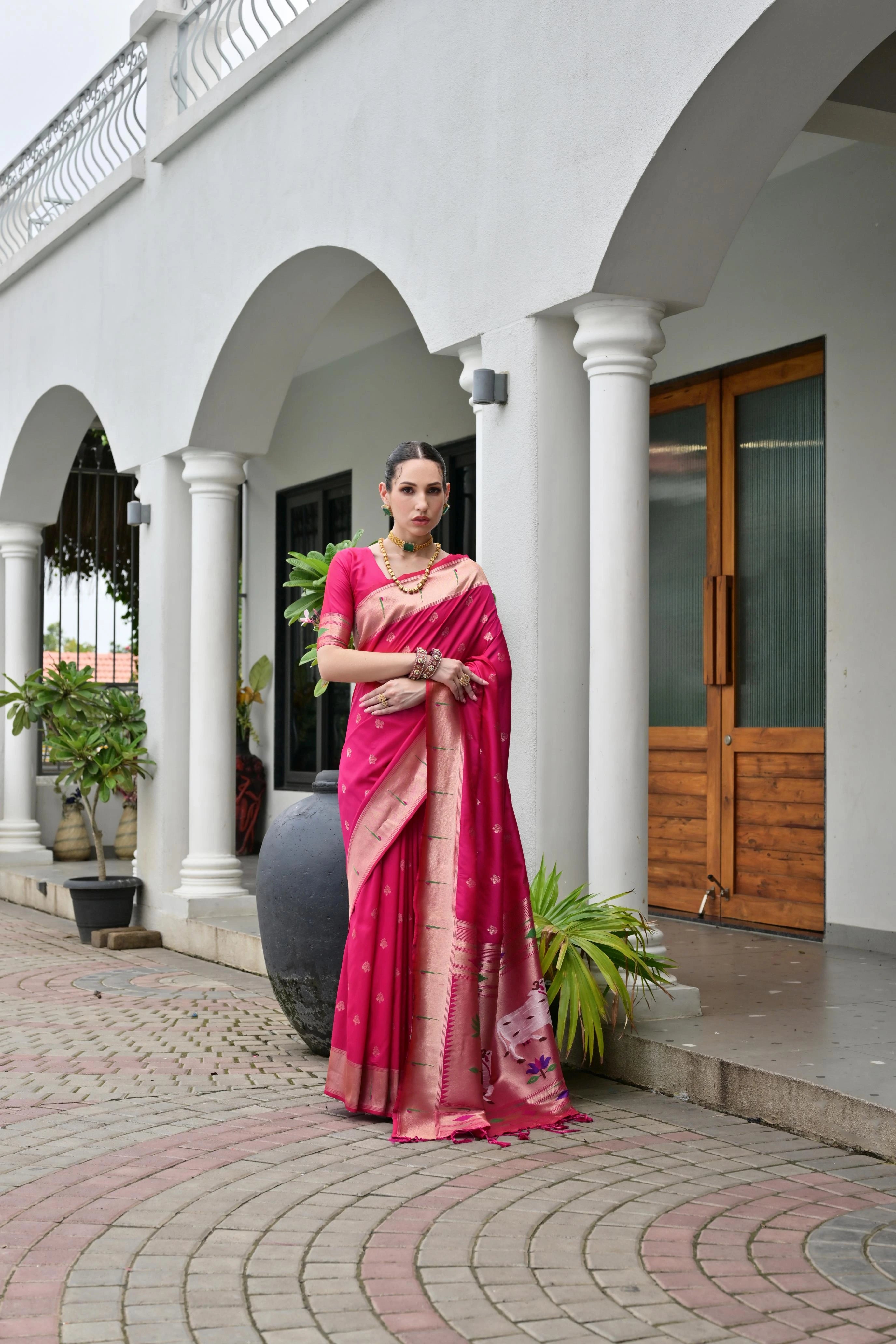Woman in a pink saree standing in front of a white building with arches.