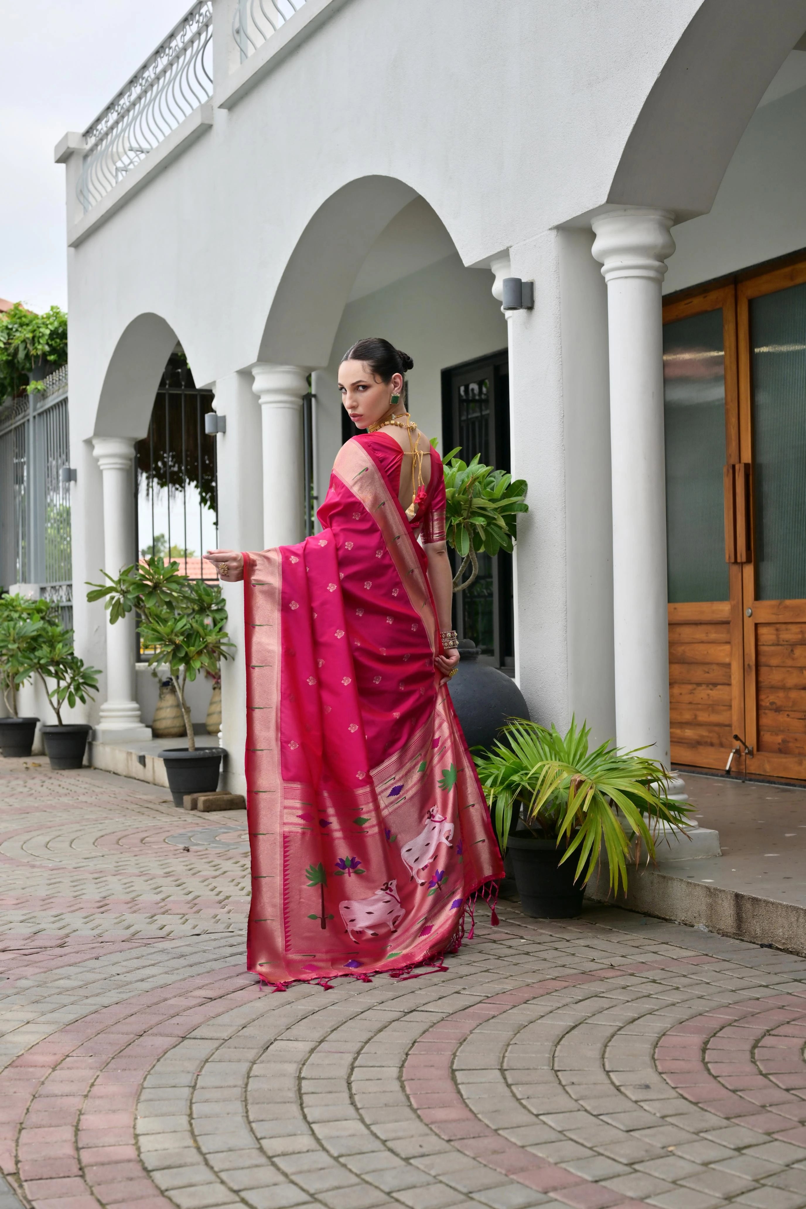 Woman in a pink saree standing in front of a white building with columns.