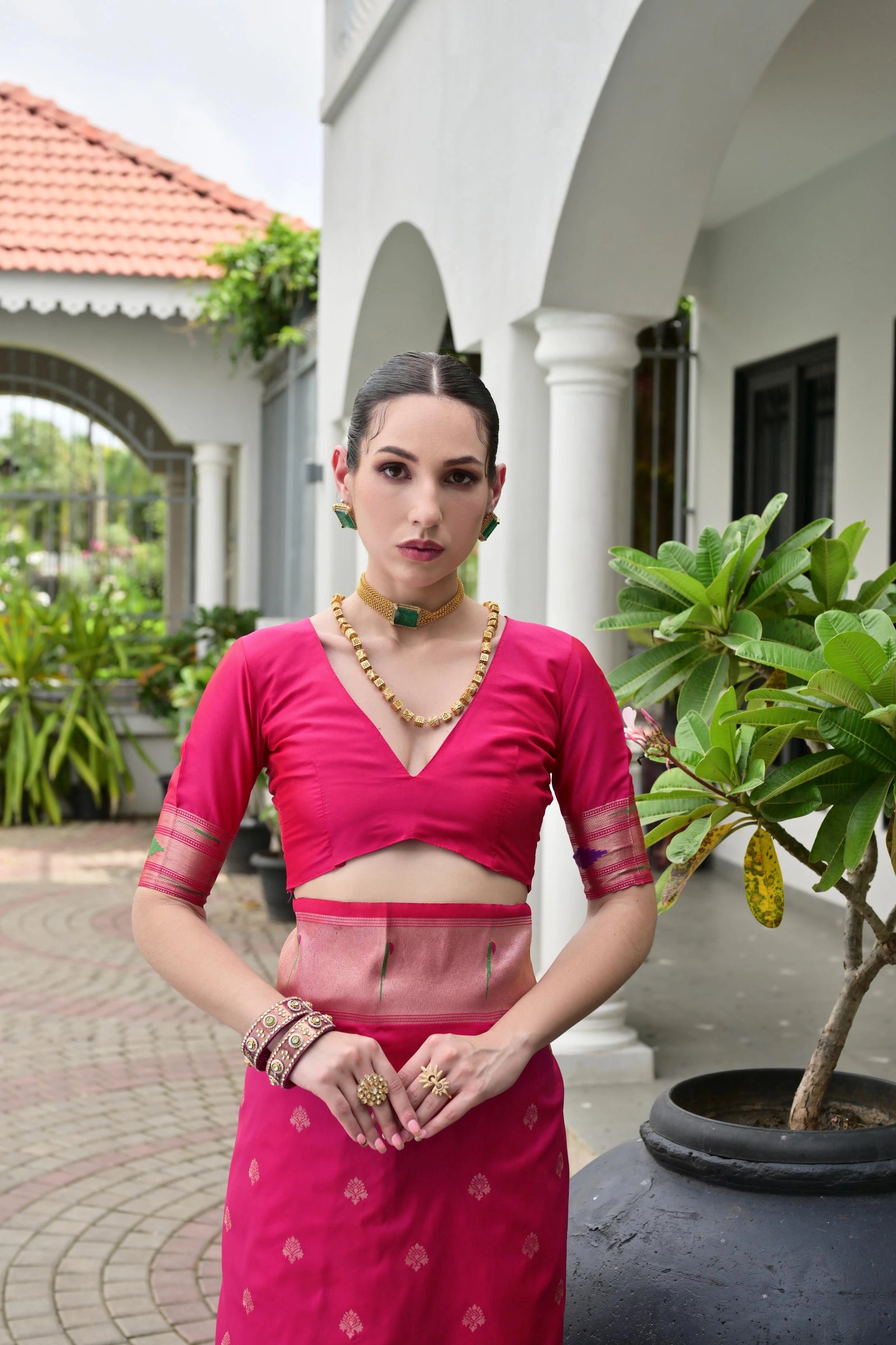 Woman in a pink traditional outfit standing in front of a white building with greenery.