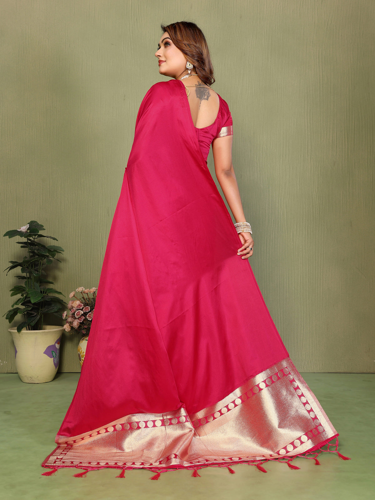 Woman wearing a pink saree with a gold border against a green background