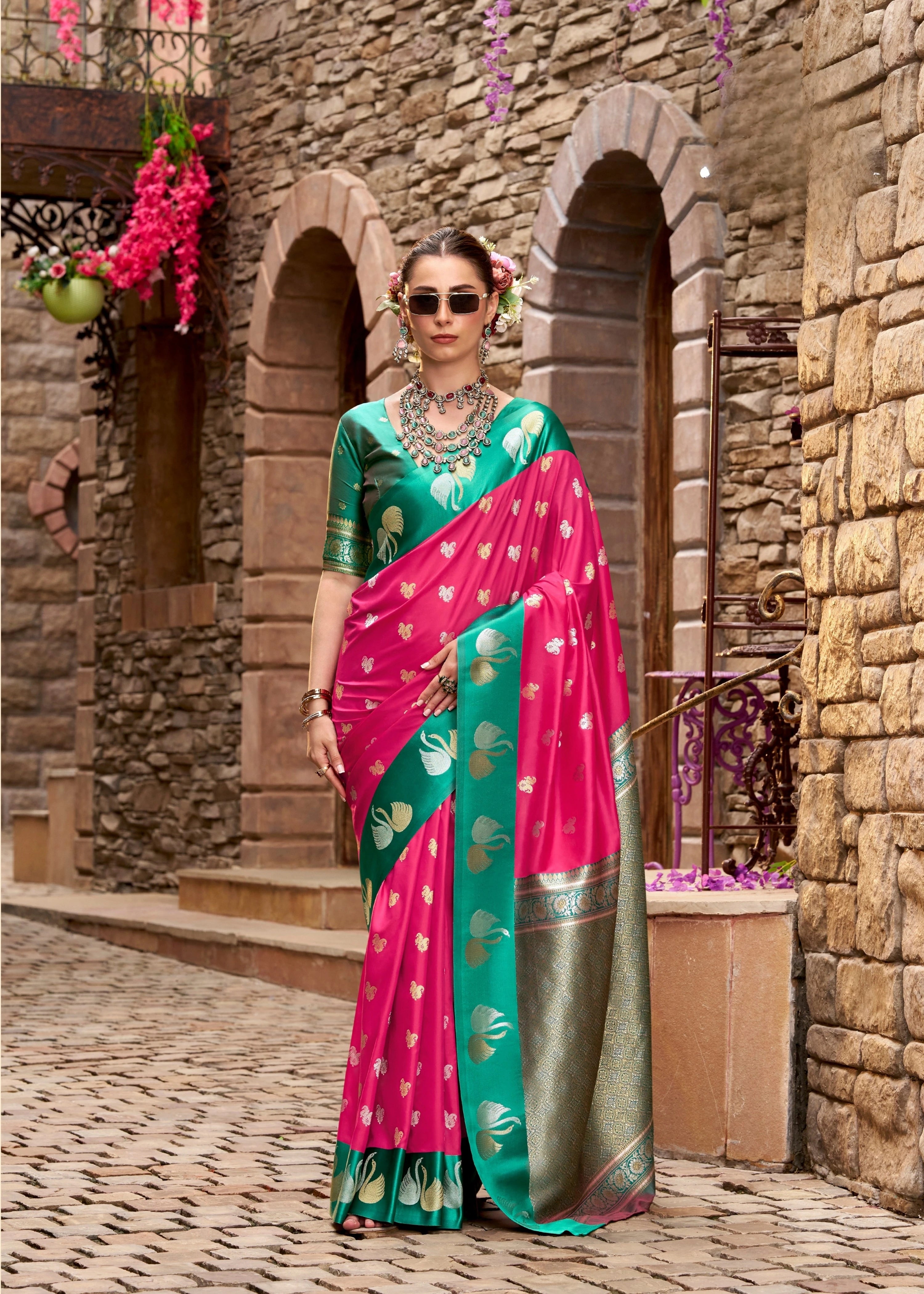 Woman in a pink and green saree standing in front of a stone building with arches.