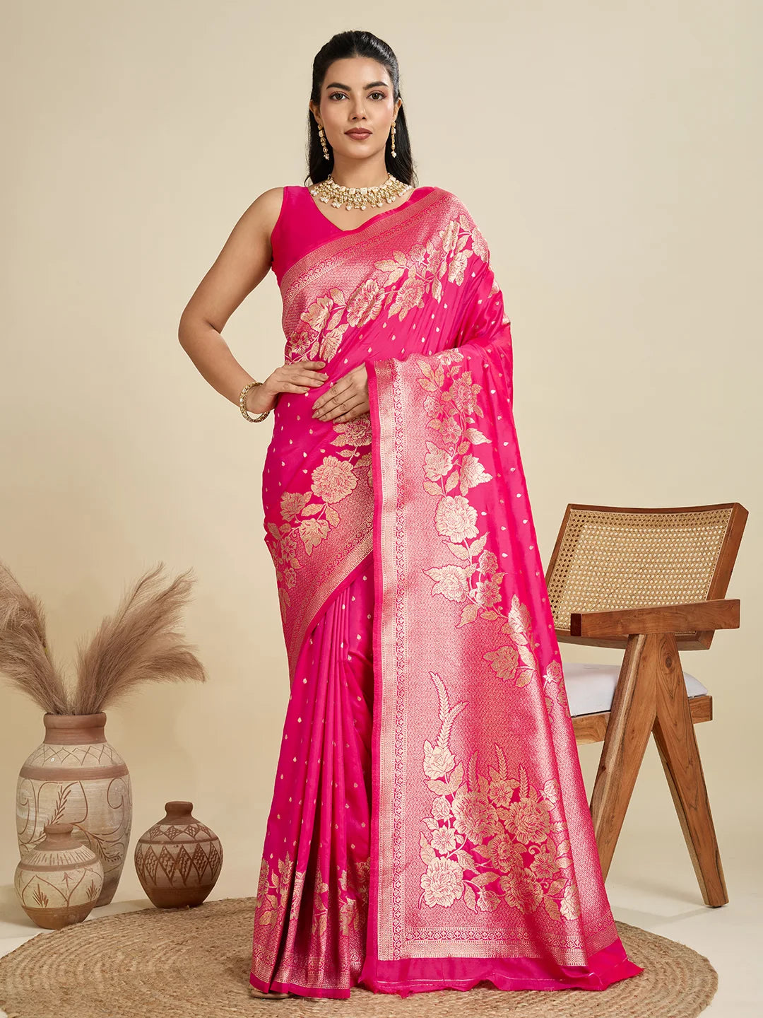 Woman wearing a pink saree with gold patterns in a minimalistic setting.