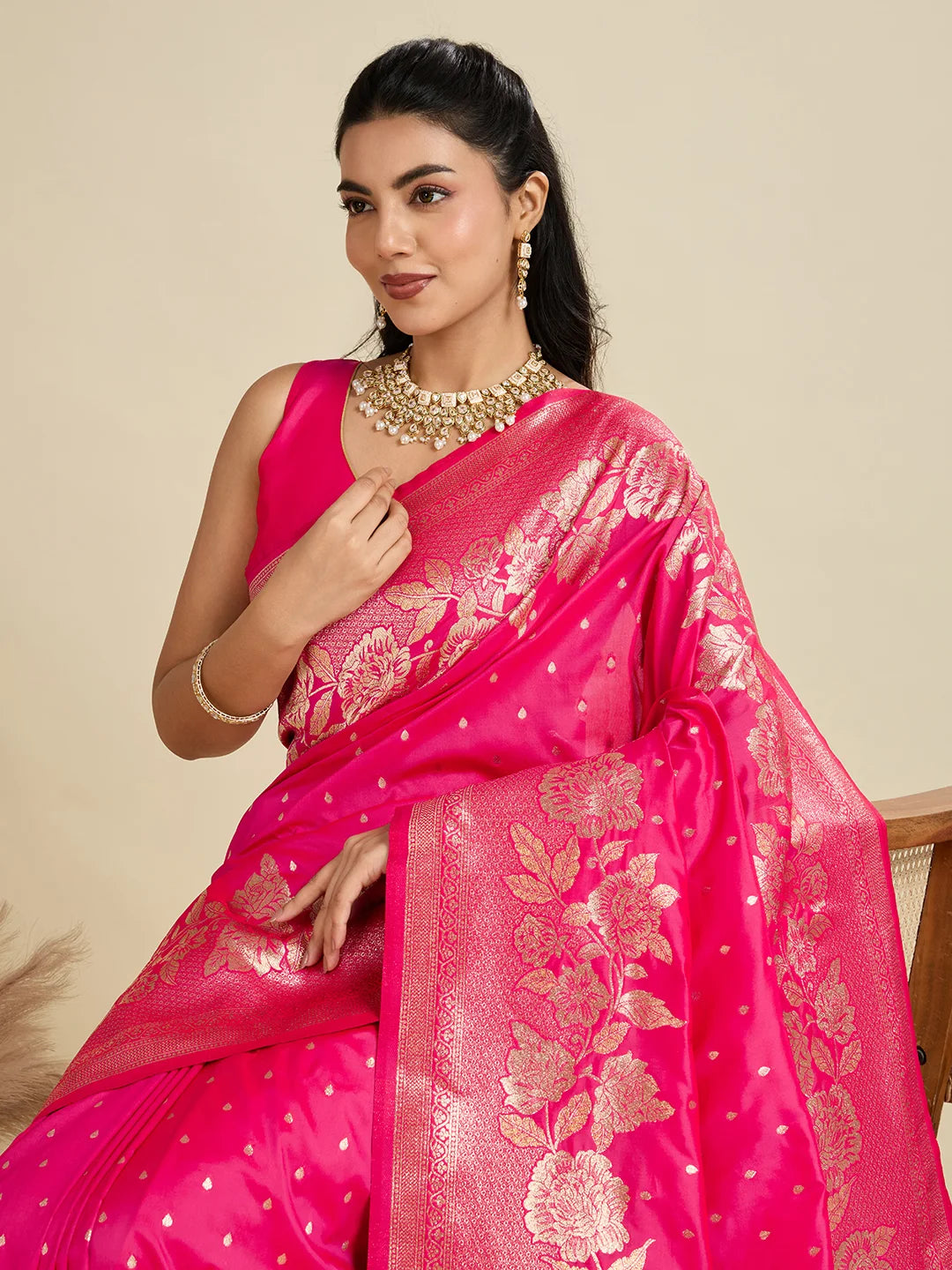 Woman wearing a bright pink saree with gold patterns on a beige background