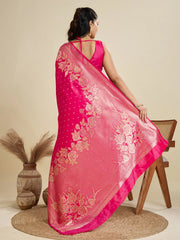 Woman wearing a pink saree with floral patterns, sitting on a chair against a beige background.