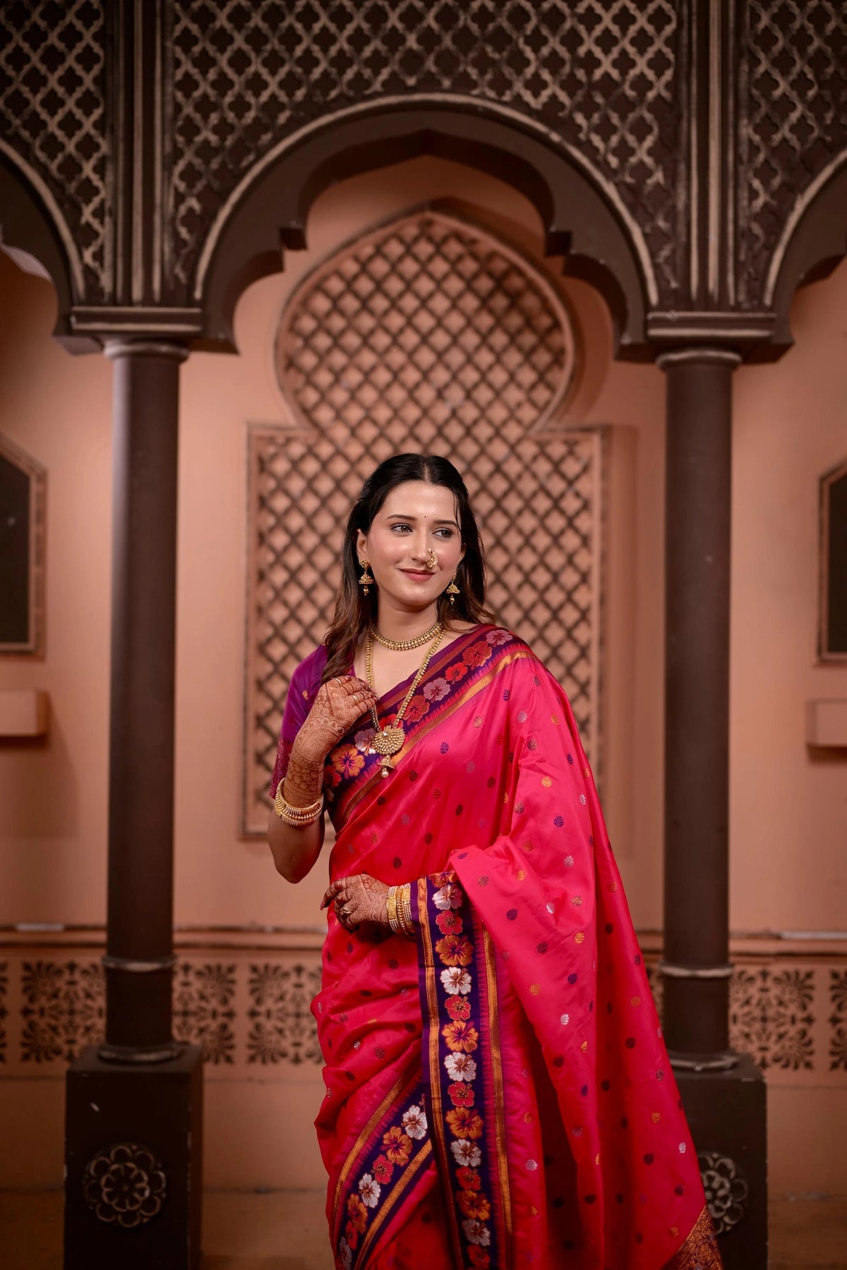 Woman in a pink saree standing in an ornate architectural setting