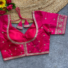 Pink embroidered blouse with gold detailing on a textured surface with flowers.