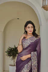 Woman in a purple saree with white patterns standing in an archway.