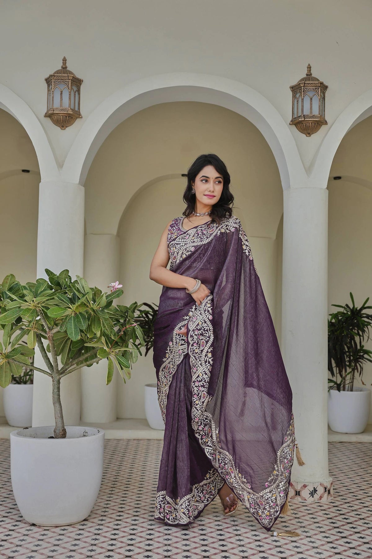 Woman in a purple saree standing in an archway with plants around
