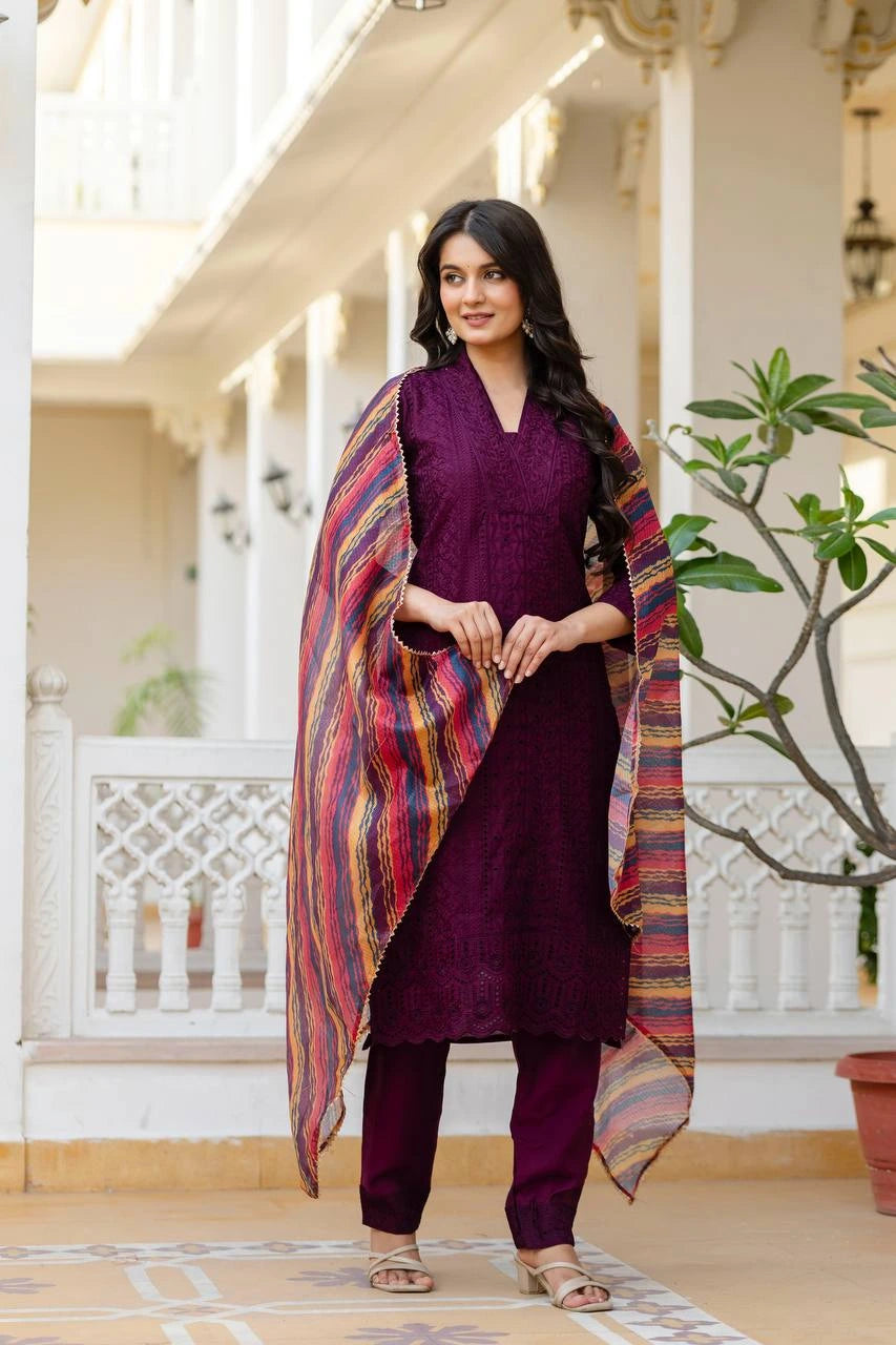 Woman in a purple outfit with a colorful scarf standing in a decorative outdoor setting.
