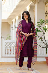 Woman in a purple outfit with a colorful scarf standing in a decorative outdoor setting.