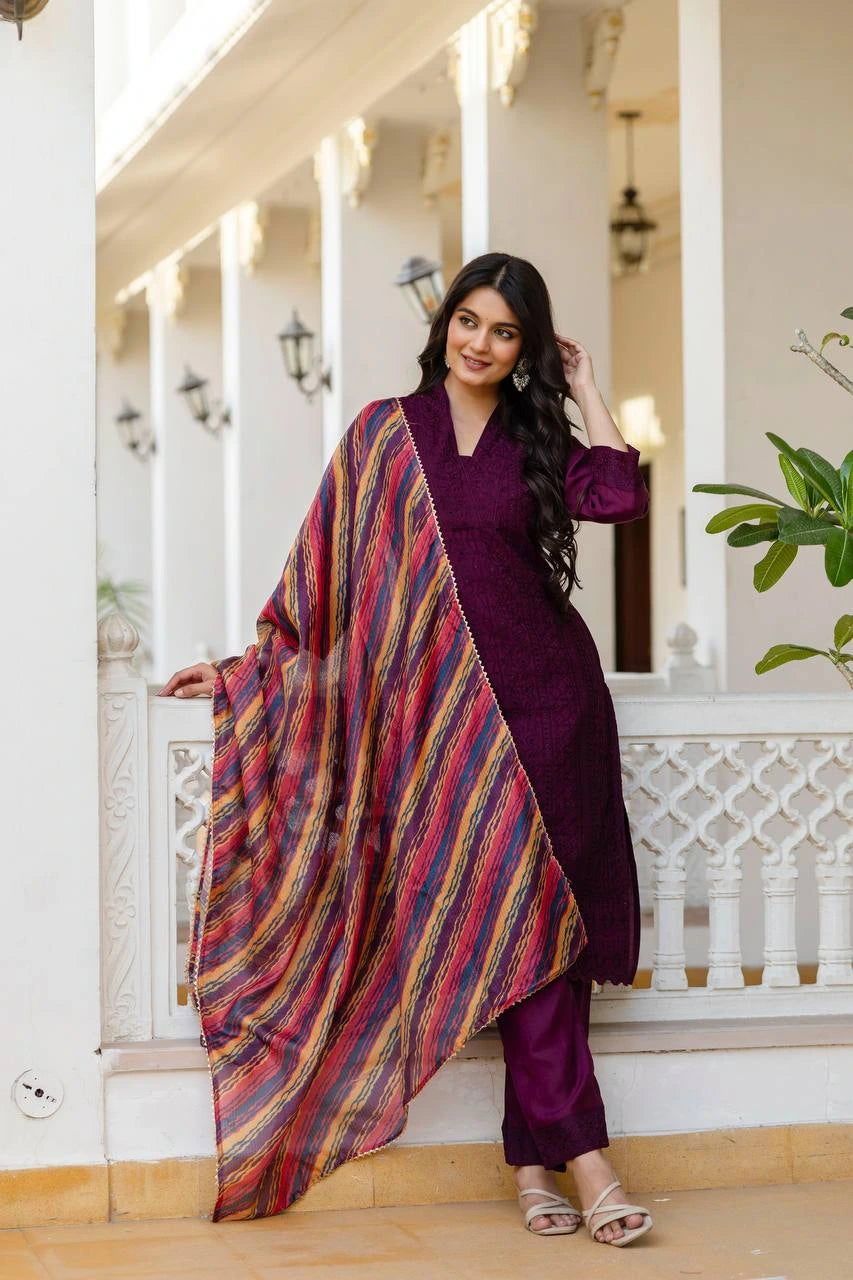Woman in a purple outfit with a colorful scarf standing in a decorative indoor setting.