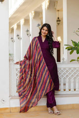 Woman in a purple outfit with a colorful scarf standing in a decorative indoor setting.