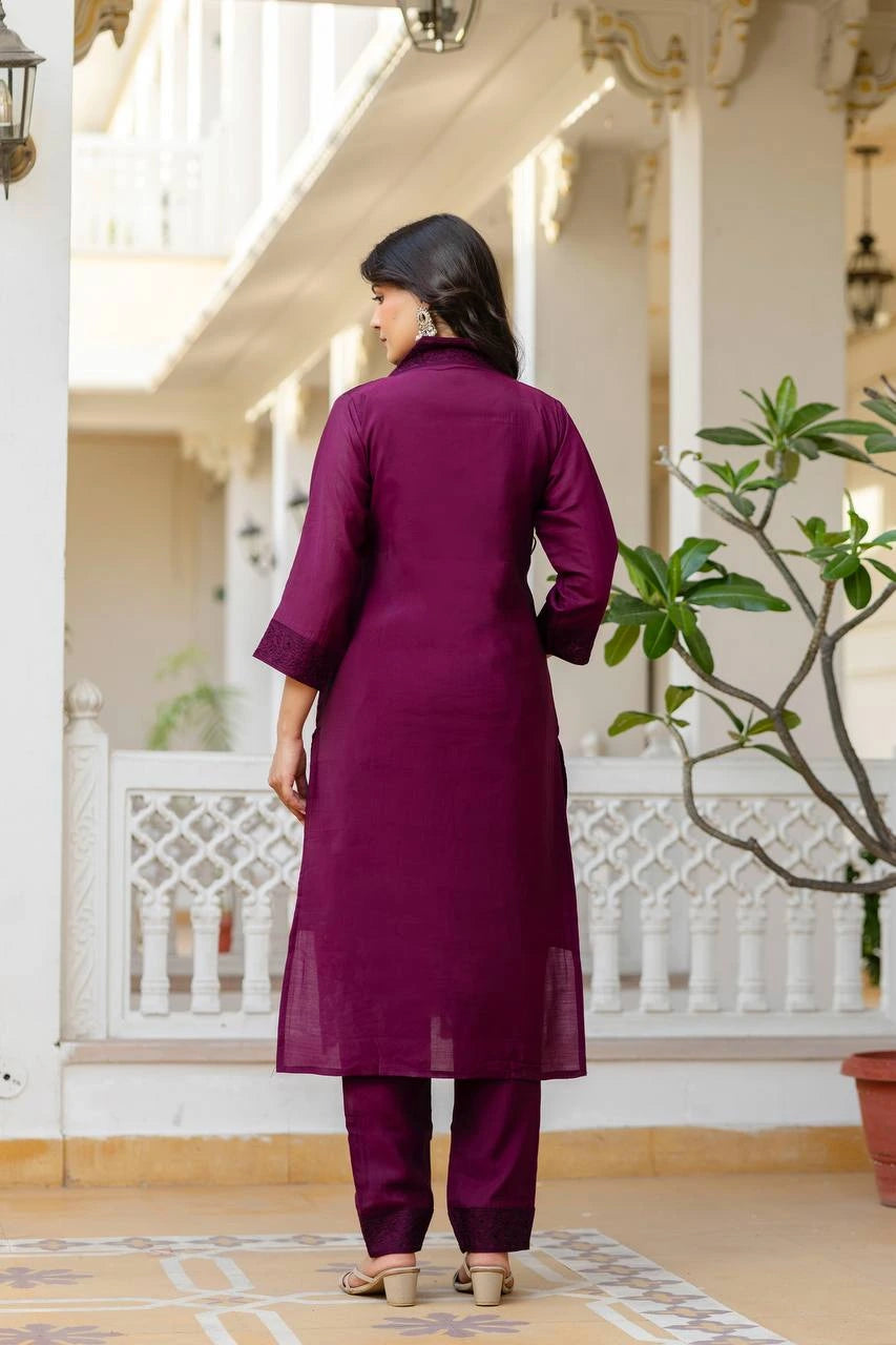 Woman in a purple outfit standing on a porch with white columns and a plant.