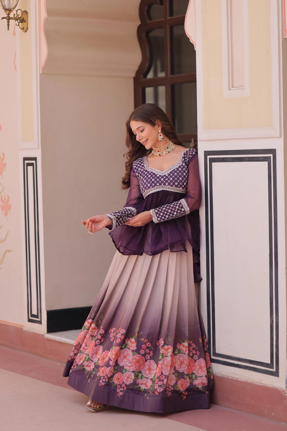 Woman in a traditional outfit with floral design standing in a decorative doorway.
