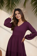 Woman wearing a purple dress with long sleeves against a neutral background