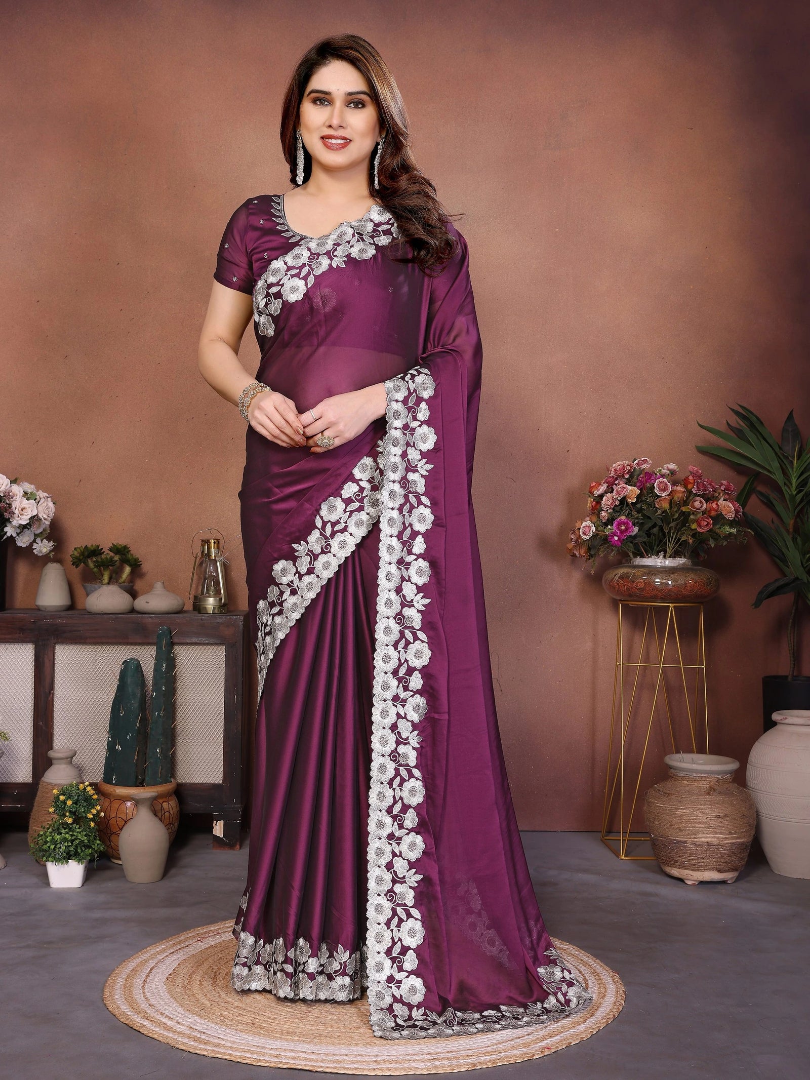Woman wearing a purple saree with white floral patterns in a decorated indoor setting.