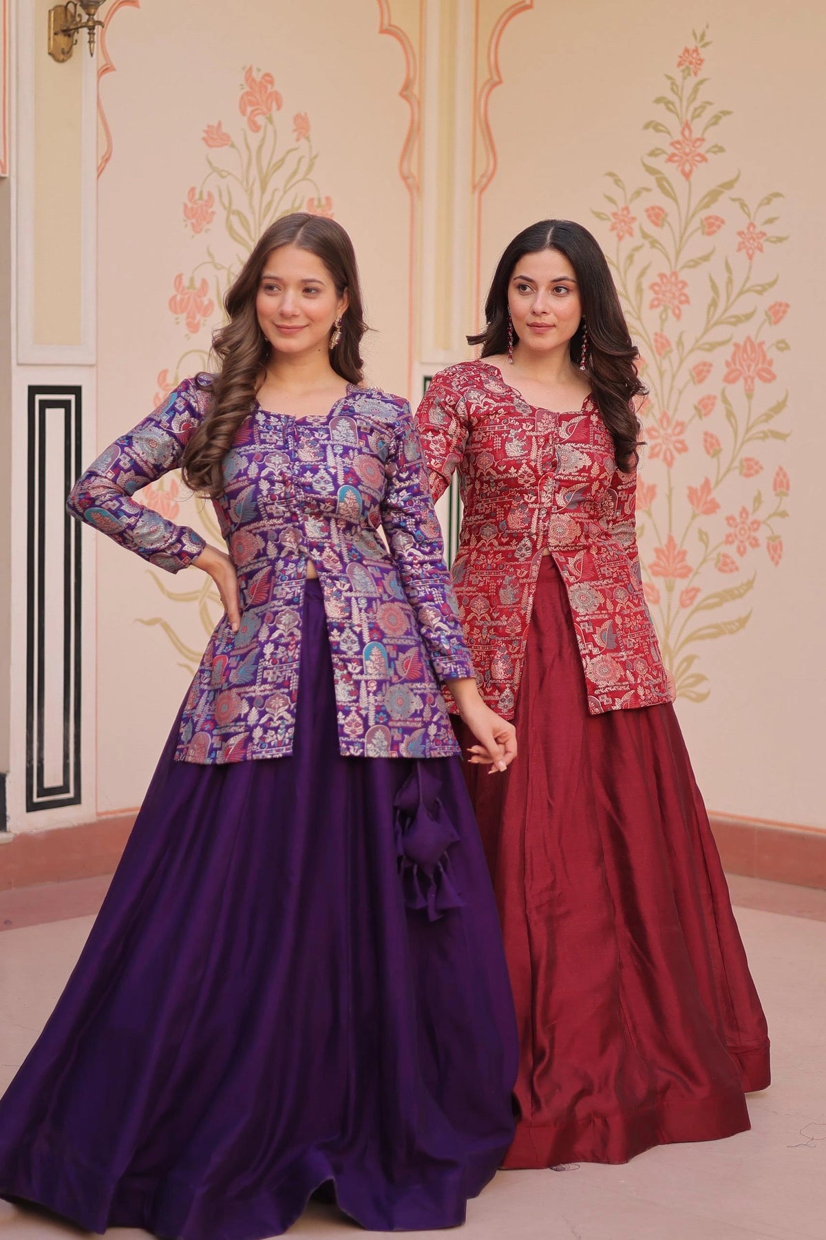 Two women wearing patterned tops and long skirts standing in a decorated room.