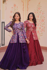 Two women wearing patterned tops and long skirts standing in a decorated room.