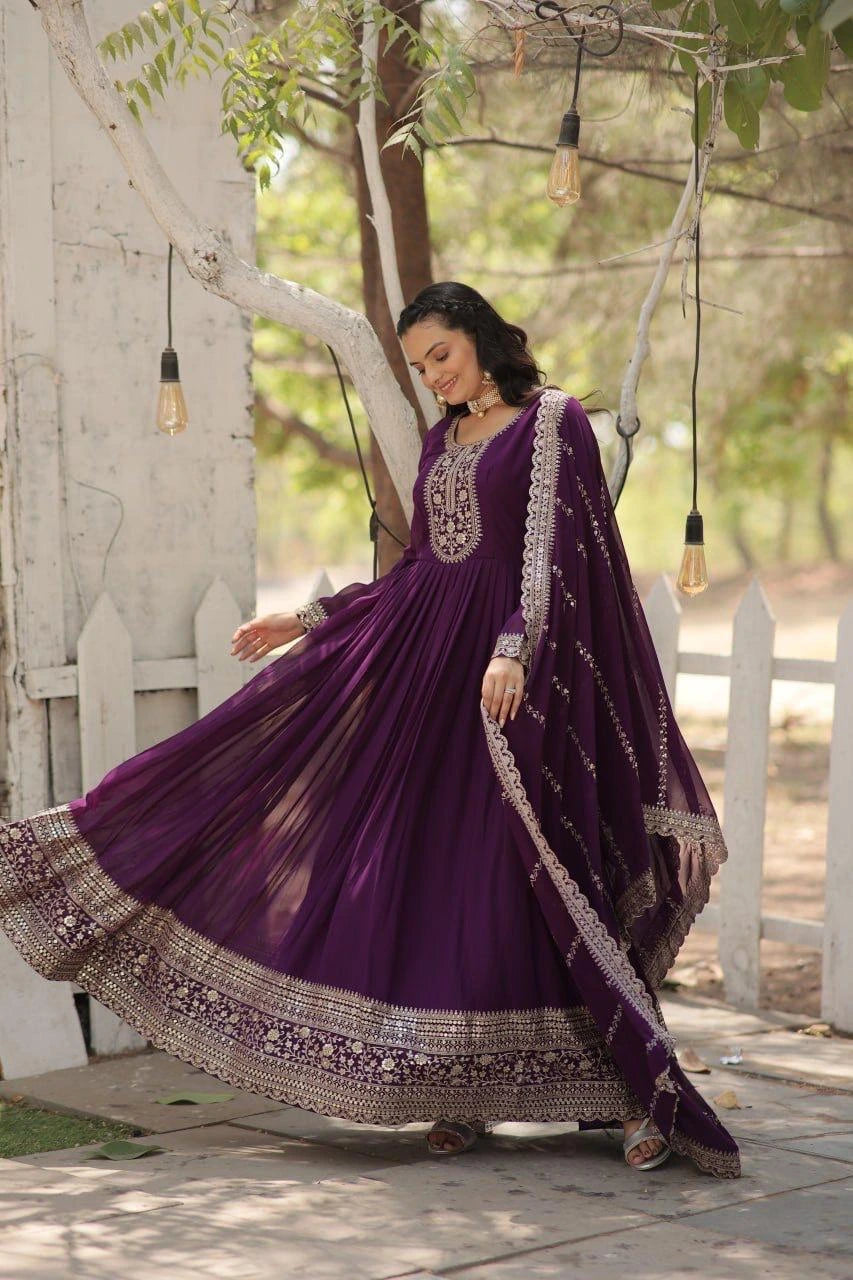 Woman in a purple traditional outfit with intricate designs standing outdoors.