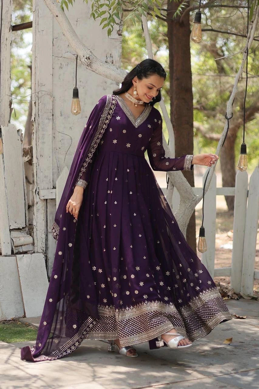 Woman in a purple traditional outfit standing outdoors with greenery in the background