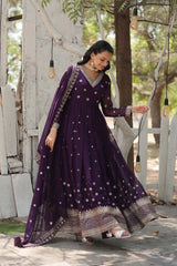 Woman in a purple traditional outfit standing outdoors with greenery in the background