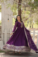 Woman in a purple traditional outfit standing outdoors with trees and a white fence in the background.